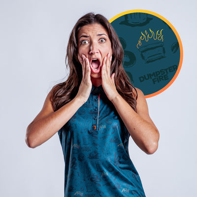 A shocked woman with long brown hair holds her face, wearing the Deep Trouble - Women's Polo, an athletic fit teal patterned sleeveless shirt. Behind her is a circular flaming dumpster graphic with "DUMPSTER FIRE" on a dark blue background.