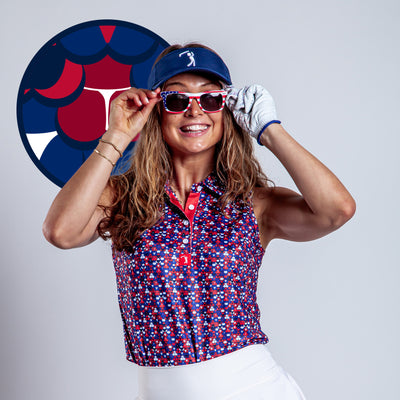 A smiling woman golfer in a blue visor, pink sunglasses, and the Whale Tail - Freedom Cheeks Women's Polo with athletic fit adjusts her glasses. She wears a golf glove and stands before blue, red, and white circular graphics.