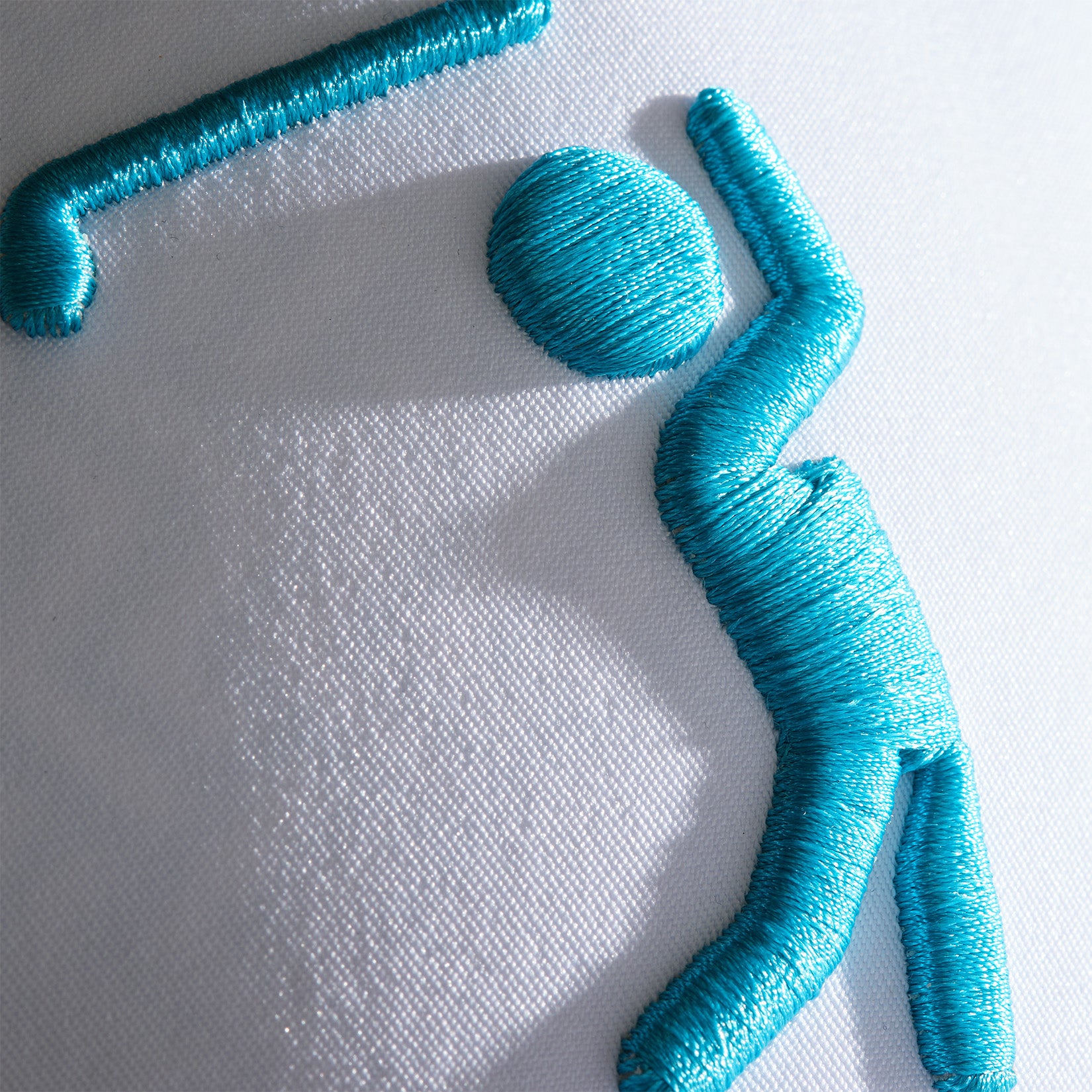 Close-up of turquoise embroidery on the Bogeyman White/Teal Performance Golf Hat (Snapback) shows a stick-figure swinging a bat. Crafted on sleek, smooth performance material, the shiny threads stand out against the white background.