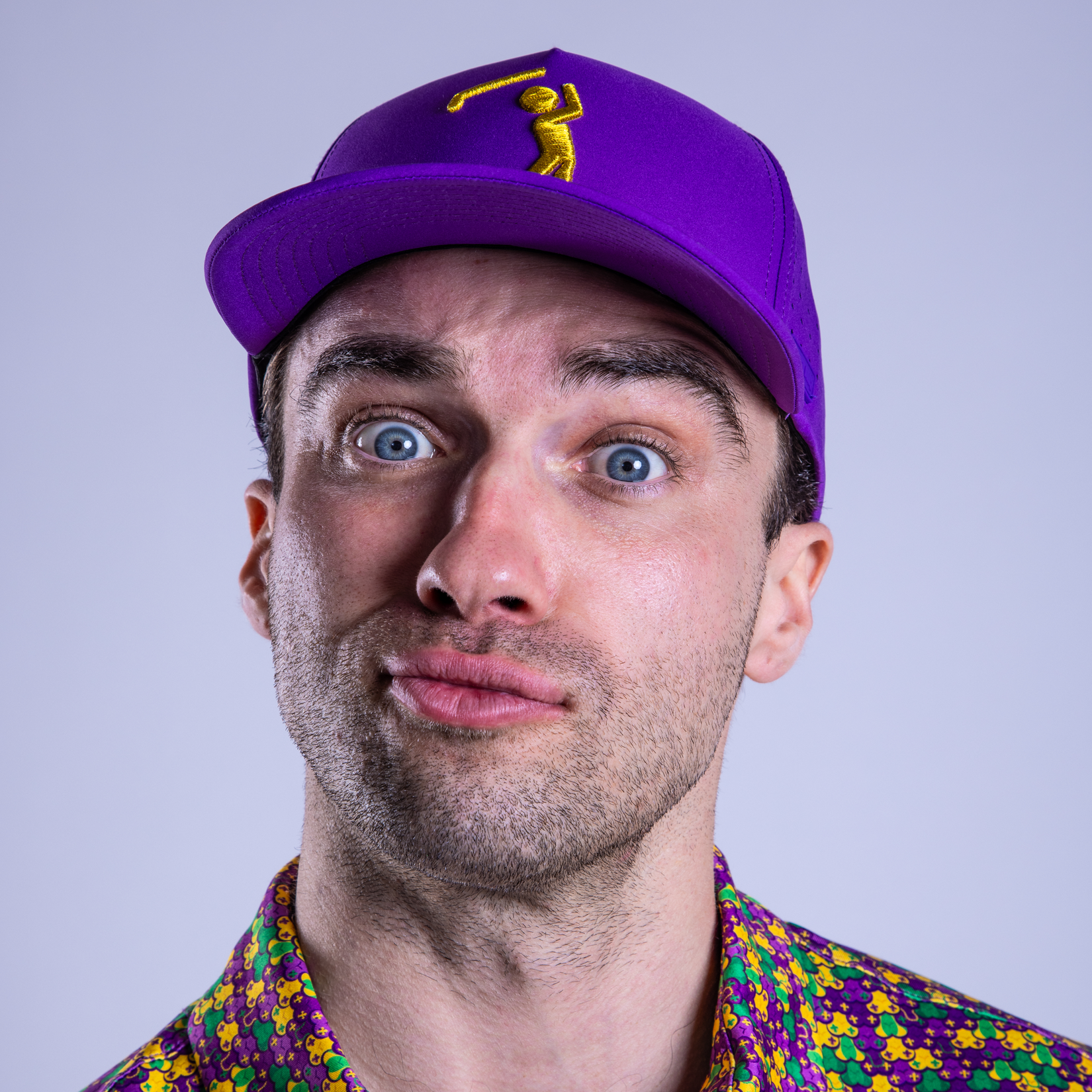 Man wearing a purple cap with a logo and a colorful shirt on a light gray background