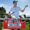 A man in a golf cap and patterned shirt holds a golf club, standing behind a set of clubs displayed on a stand. A red sign reads FOR SALE GOLF CLUBS ANY OFFER WILL BE CONSIDERED. Headcovers and clubs are visible in front of him.
