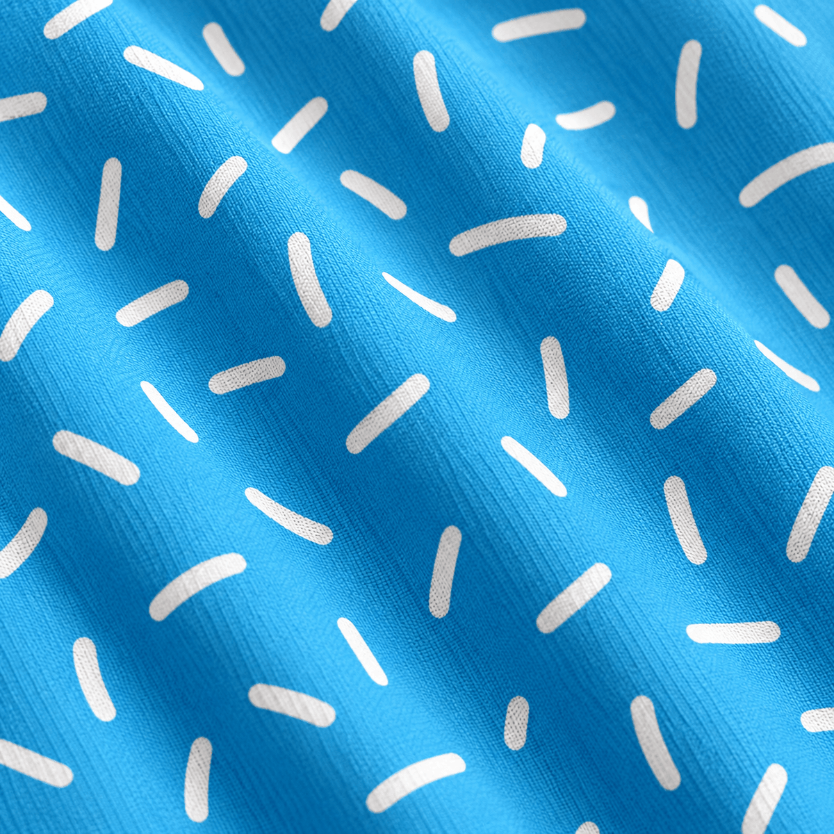 A close-up of folded Bitty Bombs - Women’s Polo fabric in vibrant blue, featuring a repeating pattern of small, white, slightly curved dash marks or sprinkles scattered across the surface. The material has a visible woven texture and offers UPF 50 protection, while the folds create subtle shadows that add depth to the polo’s bright blue appearance.