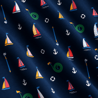 Close-up of the “Boats and Hose - Polo” fabric in navy blue, showcasing a repeating nautical pattern. Motifs include colorful sailboats with striped or dotted sails, white anchors, black and white lifebuoys, green coiled garden hoses, and blue-handled garden hoes. The soft fabric drapes in gentle folds for added depth and provides UPF 50 protection for enhanced sun safety.