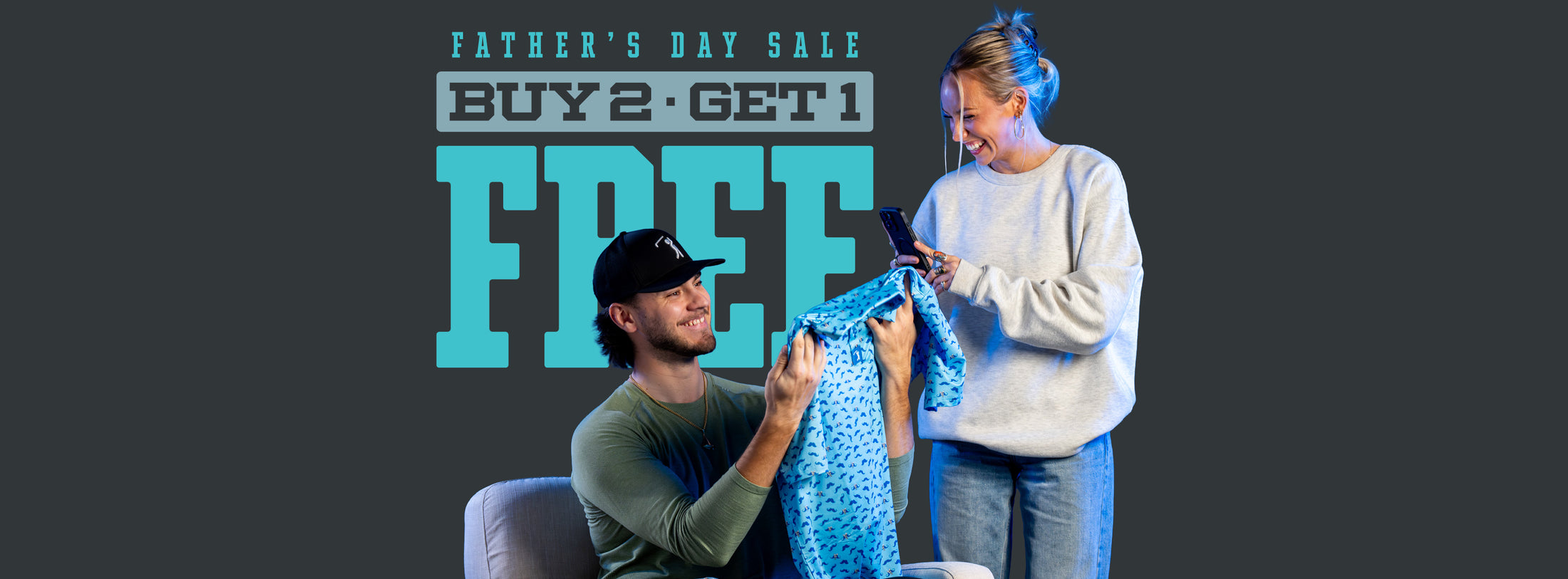 A smiling man in a cap sits in a chair holding up a blue patterned shirt, while a woman in a gray sweatshirt stands next to him, smiling and holding a phone. Large text behind them reads: Father’s Day Sale. Buy 2 - Get 1 FREE.