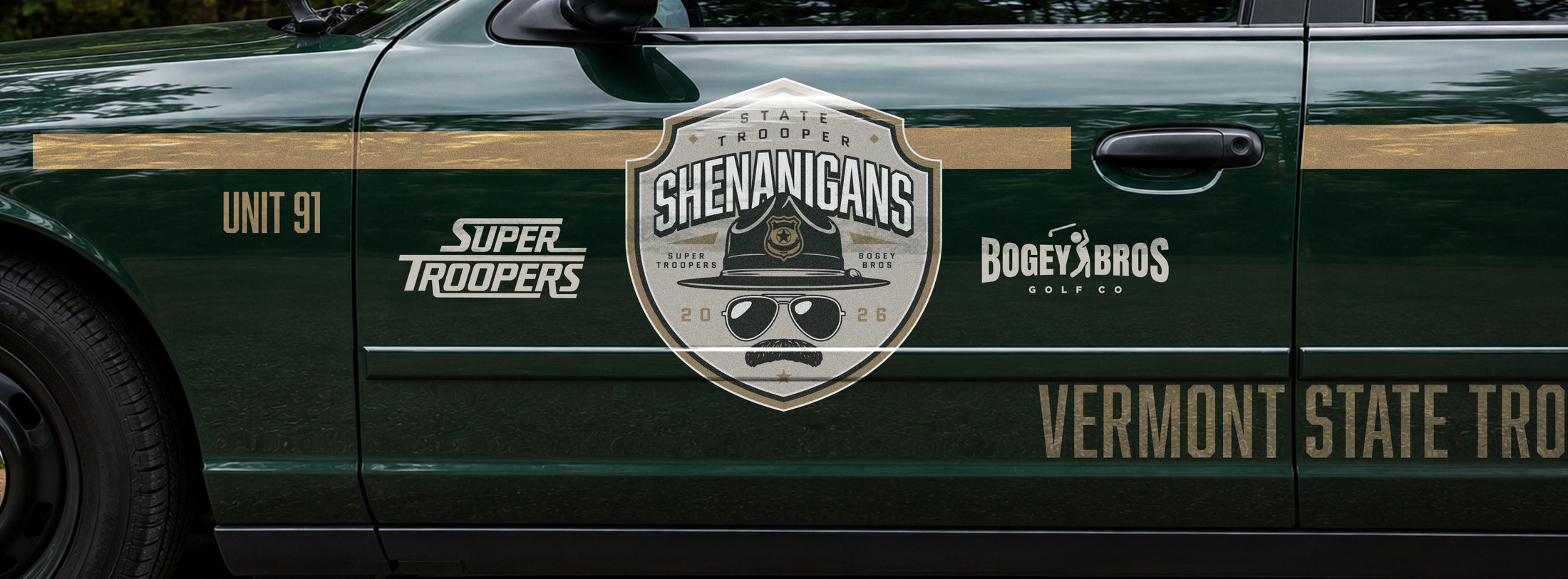 Side of a dark green police car with a large badge logo reading Shenanigans featuring a mustache and sunglasses, surrounded by sponsors Super Troopers and Bogey Bros Golf Co. Text also reads Vermont State Troopers, Unit 91, and Vermont State Police..
