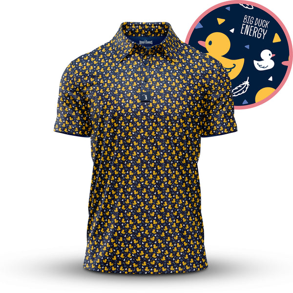 The “Big Duck Energy - Polo” is a navy athletic-fit shirt featuring a repeating yellow rubber duck pattern, with close-up insets highlighting playful ducks, leaves, waves, and “BIG DUCK ENERGY” text on a dark background.