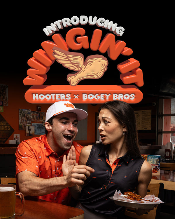 A cheerful man in an orange shirt excitedly gestures to a surprised woman holding hot wings at a restaurant table. Above them, bold text reads “Introducing Wingin’ It – Hooters x Bogey Bros,” with a winged chicken drumstick logo.