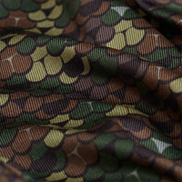 A close-up of the Whale Tail - Camo - Polo shows scalloped, scale-like patterns in green, brown, and tan. The ribbed, moisture-wicking fabric adds depth and comfort, with a camouflage look reminiscent of reptile skin.