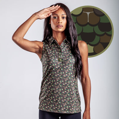 A woman with long dark hair wears the Whale Tail - Camo - Women's Polo, featuring a sleeveless, super stretchy camouflage pattern. She stands saluting with her right hand before a circular green and brown camo scale graphic.